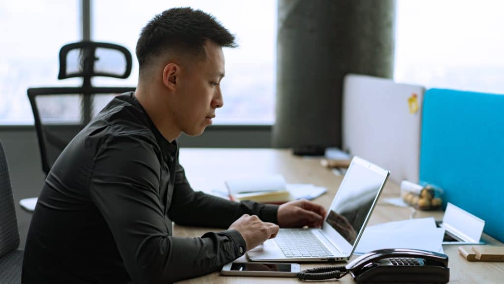 A Man Sitting At A Desk Using A Laptop